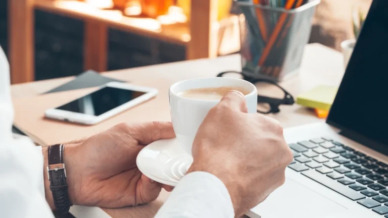 Lange Arbeitstage: Hände mit Kaffeetasse am Schreibtisch als kurze Erholung zwischen der Arbeit