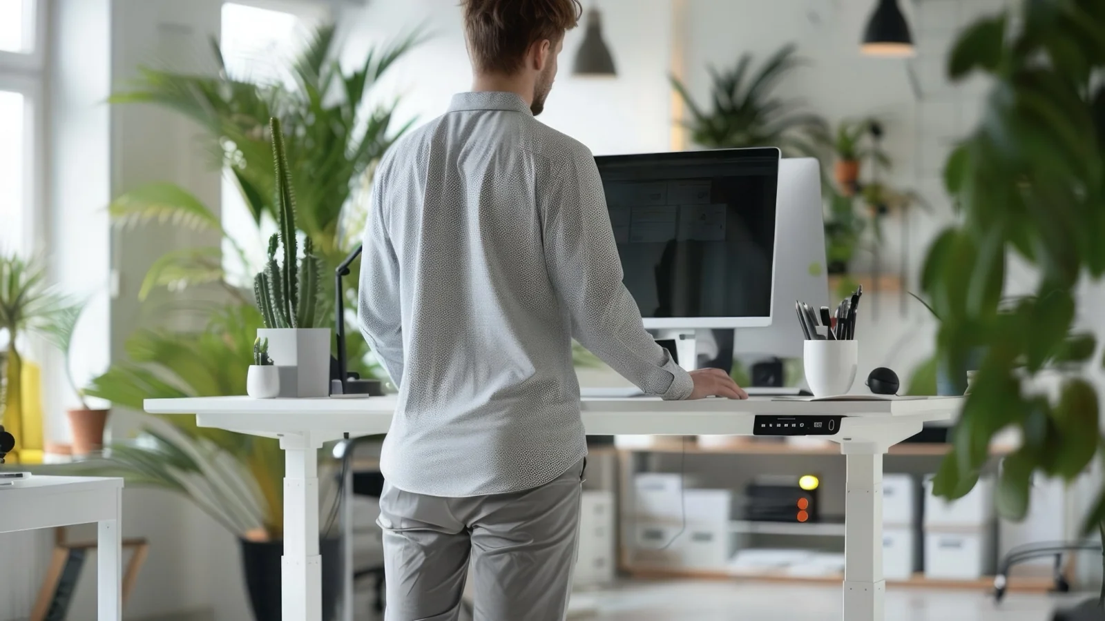 Bildschirmarbeit-Unterbrechung: Person steht am Schreibtisch mit Monitor als Hinweis auf kurze Entlastung