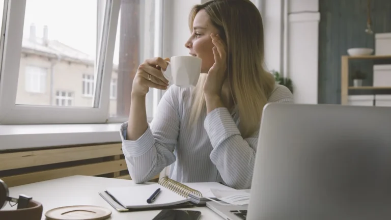 5-Minuten-Pause im Büro: Person mit Kaffeetasse blickt am Schreibtisch kurz aus dem Fenster